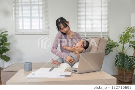Mother multitasking on the phone while holding her baby in a cozy home office. 122716695