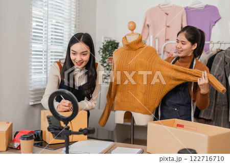 Two diverse retail workers showcasing a sweater while managing inventory and recording content. 122716710