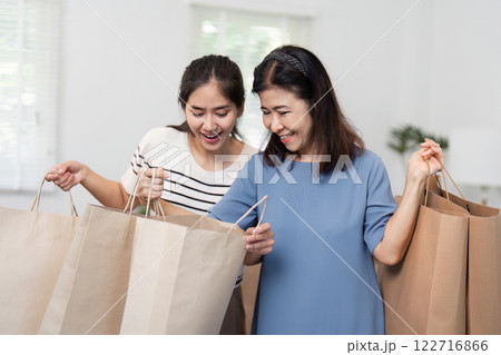 Excited daughter and mother exploring their shopping bags together, sharing a joyful moment 122716866