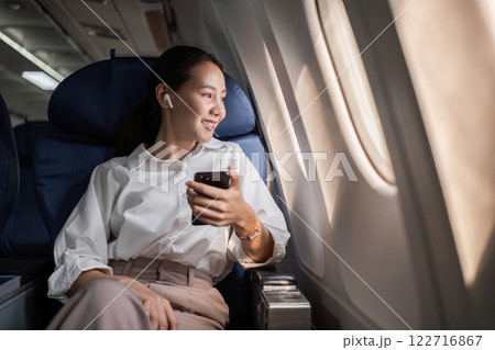 Business Woman Traveling by Plane, Relaxing in Comfortable Seat, Using Smartphone, Enjoying In-Flight Experience, Modern Air Travel Concept 122716867