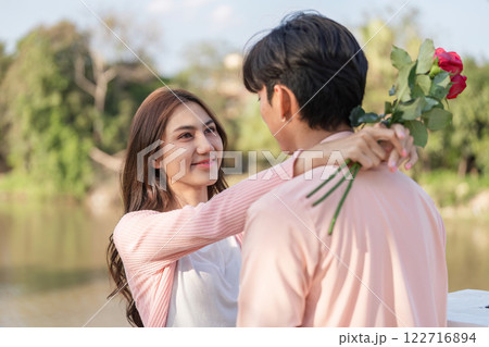 Romantic couple celebrating Valentines Day by the riverside, sharing love and roses in a picturesque setting 122716894