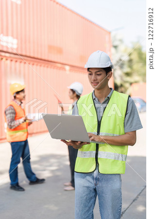 Construction worker using a laptop to manage projects while colleagues discuss plans on-site 122716912