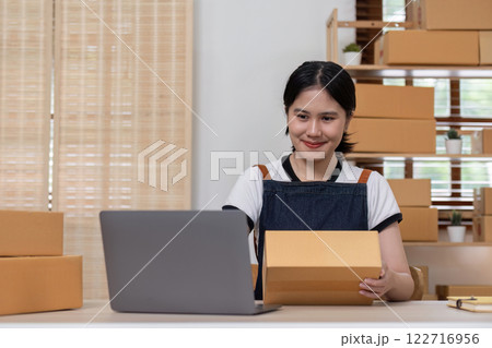 young female entrepreneur writes on the front of a product box to sell products online and prepares to send them to customers. Online selling at home, working from home 122716956