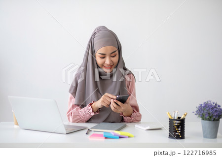 Smiling Muslim business woman Wearing a hijab while chatting online on a work desk in the office. 122716985