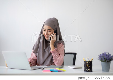 Smiling Muslim business woman Wearing a hijab while chatting online on a work desk in the office. 122716999