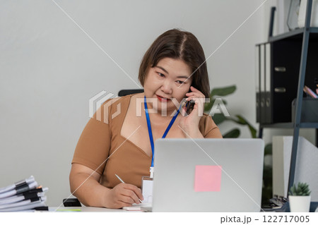 Businesswomen communicating on the phone while taking notes in a contemporary office setting 122717005