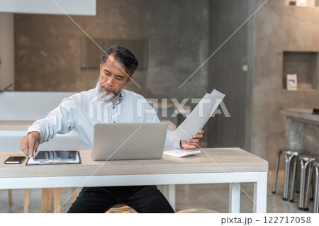 Engaged male businessman coordinating documents while using laptop in a sleek modern workspace Engaged male businessman coordinating documents while using laptop in a sleek modern workspace 122717058