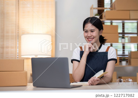 young female entrepreneur writes on the front of a product box to sell products online and prepares to send them to customers. Online selling at home, working from home 122717082