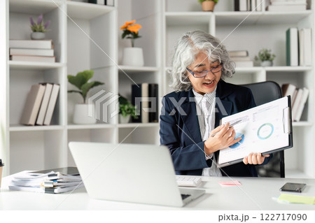 Senior Businesswoman Conducting Online Presentation with Graphs in Modern Office Setting Senior Businesswoman Conducting Online Presentation with Graphs in Modern Office Setting 122717090