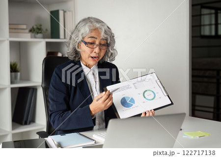 Senior Businesswoman Conducting Online Presentation with Graphs in Modern Office Setting 122717138