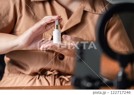 Young woman showcasing skincare serum during a live stream, engaging with viewers as a beauty influencer Young woman showcasing skincare serum during a live stream, engaging with viewers as a beauty influencer 122717246