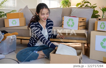 A young woman separates unused clothes and prepares them for donation or recycling in order to reduce air pollution and protect the environment. 122717284