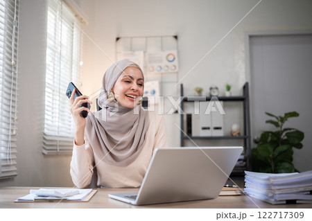 Muslim female entrepreneur wearing hijab sits working with laptop managing personal business in private office. Muslim female entrepreneur wearing hijab sits working with laptop managing personal business in private office. 122717309