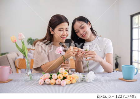Middle-aged daughter happily arranges flowers with her mother at home Free time activities that are done together as a family Middle-aged daughter happily arranges flowers with her mother at home Free time activities that are done together as a family 122717405