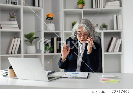 Elderly business woman discussing strategies on a phone call while reviewing documents in a modern office 122717407