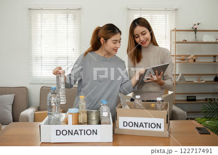 Two young female volunteers help pack food into donation boxes and prepare to donate them to charity. 122717491