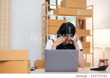A young female entrepreneur feels stressed about selling products online and preparing to send them to customers. Online selling at home, working from home A young female entrepreneur feels stressed about selling products online and preparing to send them to customers. Online selling at home, working from home 122717552