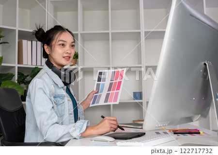 Female designer wearing headphones listening to music while doing graphic design work Choose colors for working with the computer at the table. Female designer wearing headphones listening to music while doing graphic design work Choose colors for working with the computer at the table. 122717732