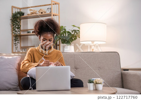 Young African Woman Relaxing at Home While Working Online with Laptop and Headphones in Cozy Living Room Setting Young African Woman Relaxing at Home While Working Online with Laptop and Headphones in Cozy Living Room Setting 122717760
