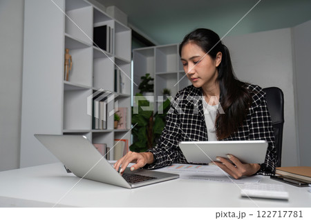 Dedicated Businesswoman Working Late Hours in Modern Office with Laptop and Tablet 122717781