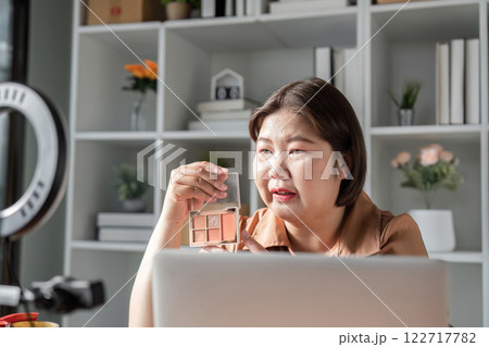 E-commerce entrepreneur explaining features of eyeshadow palette while engaging viewers during live stream from home office 122717782