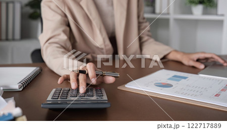 Young female accountant is calculating business and financial figures using a calculator. On the wooden table in the office 122717889