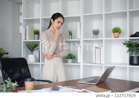 Asian businesswoman feeling tired and stressed over an unsuccessful business while working in a home office decorated with soothing green plants. 122717929