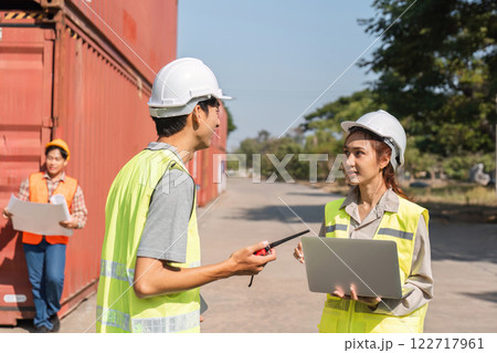 Construction team engaged in discussion and planning near shipping containers in a busy site Construction team engaged in discussion and planning near shipping containers in a busy site 122717961