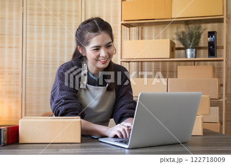 Young Asian female online business entrepreneur is searching customer information on laptop and packing products on table to ship to customer. 122718009
