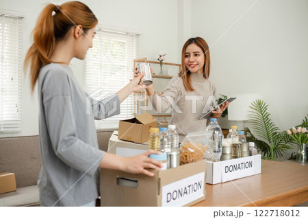Two young female volunteers help pack food into donation boxes and prepare to donate them to charity. Two young female volunteers help pack food into donation boxes and prepare to donate them to charity. 122718012