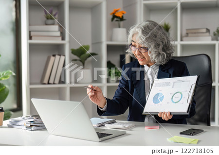 Senior Businesswoman Conducting Online Presentation with Graphs in Modern Office Setting for Virtual Meeting Senior Businesswoman Conducting Online Presentation with Graphs in Modern Office Setting for Virtual Meeting 122718105