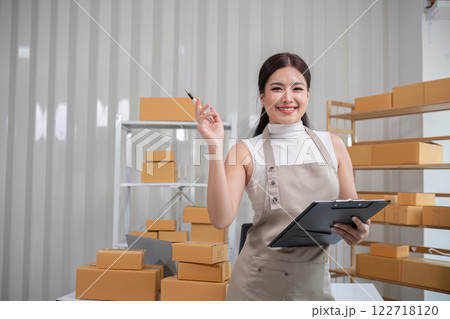 A small SME business owner writes inventory and shipping information on a clipboard in his home office. Small business operators preparing to ship to customers A small SME business owner writes inventory and shipping information on a clipboard in his home office. Small business operators preparing to ship to customers 122718120