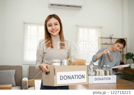 Beautiful female volunteer holds a donation box with canned food in it. Beautiful female volunteer holds a donation box with canned food in it. 122718223