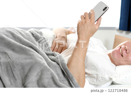 寝室でスマホを持つ笑顔の若いアジア人男性 寝室でスマホを持つ笑顔の若いアジア人男性 122718486