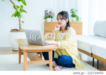 自宅でノートパソコンを操作しながら考える若い女性 122719450