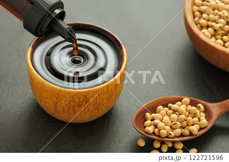 soy sauce pouring from bottle in wooden bowl with splash and drop and dry soybeans on black stone background soy sauce pouring from bottle in wooden bowl with splash and drop and dry soybeans on black stone background 122721596
