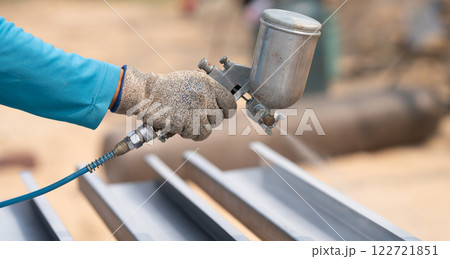 Construction worker painting metal structure surface coating with a spray gun at construction site. Metal corrosion and rust protection. Industrial precision. Protective coating to a metal structure. Construction worker painting metal structure surface coating with a spray gun at construction site. Metal corrosion and rust protection. Industrial precision. Protective coating to a metal structure. 122721851