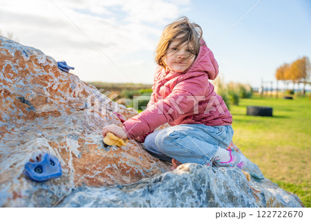 Little girl climbing an artificial climbing wall in a playground, developing strength and coordination Little girl climbing an artificial climbing wall in a playground, developing strength and coordination 122722670