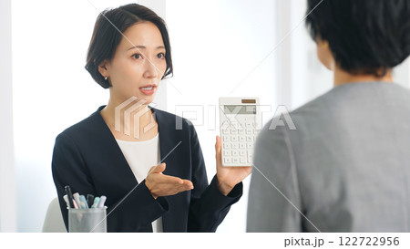 オフィスで電卓を見せて価格交渉する二人の女性ビジネスパーソン 122722956