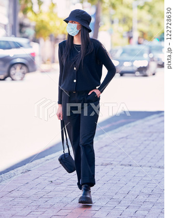 City woman, on a sidewalk, with a mask on her face and walking down the road. Urban fashion, casual walk and covid protection, life in the new normal. Calm beauty, trendy girl walks on the pavement. City woman, on a sidewalk, with a mask on her face and walking down the road. Urban fashion, casual walk and covid protection, life in the new normal. Calm beauty, trendy girl walks on the pavement. 122728630