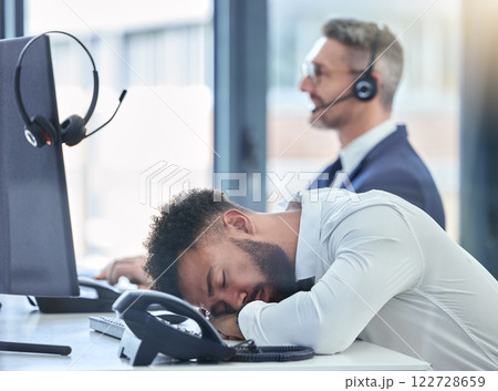 Lazy, sleeping and tired call center agent at his table or desk at work overworked suffering from burnout. Exhausted young customer service employee asleep in the office or workplace 122728659