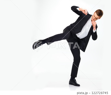 Business man doing a karate kick to the side while standing in a studio with copy space. Man in suit working on his fitness with martial arts training. Professional spy agent practicing to fight. Business man doing a karate kick to the side while standing in a studio with copy space. Man in suit working on his fitness with martial arts training. Professional spy agent practicing to fight. 122728745
