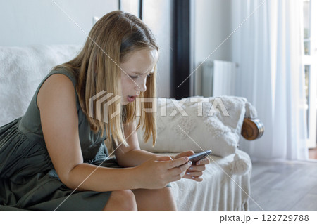 Angry little girl with smartphone watching cartoons or playing mobile games at home, indoor portrait 122729788