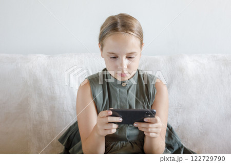 Serious little girl with smartphone watching cartoons or playing mobile games at home Serious little girl with smartphone watching cartoons or playing mobile games at home 122729790