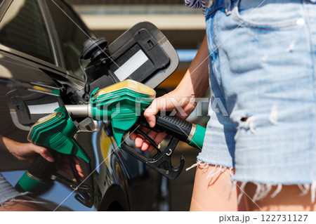 Close--up woman casual outfit hand hold fuel pump nozzle refuel car gas station sunny summer day. Confident female person filling auto tank fuel holding fuel nozzle enjoy travel vacation journey trip 122731127