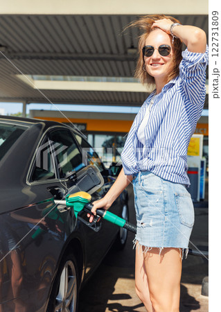 Portrait happy smiling woman sunglasses casual outfit refuel car gas station sunny summer day. Confident female person filling auto tank fuel holding fuel nozzle enjoy travel vacation journey trip 122731809
