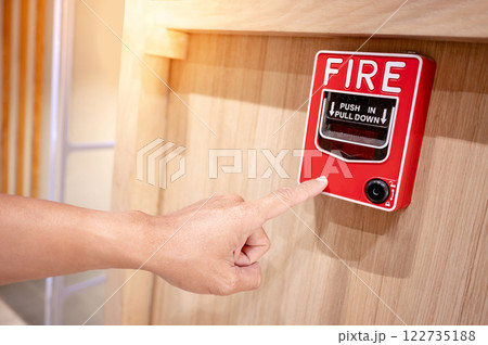 Hand pointing at red fire alarm switch mounted on wooden wall in the office interior 122735188