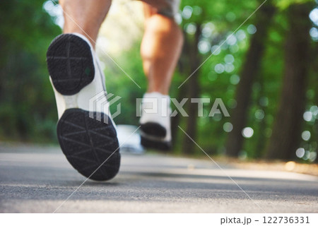 Outdoor cross-country running in concept for exercising, fitness and healthy lifestyle. Close up of feet of young runner man running along road in the park 122736331