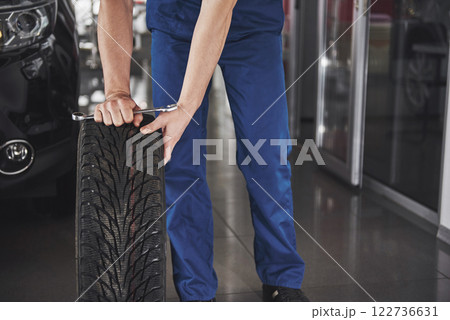 Technician with a blue workwear, holding a wrench and a tire while showing thumb up Technician with a blue workwear, holding a wrench and a tire while showing thumb up 122736631