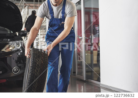 Technician with a blue workwear, holding a wrench and a tire while showing thumb up 122736632